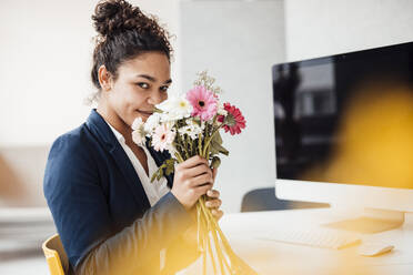 Glückliche Geschäftsfrau mit Blumen im Büro sitzend - JOSEF10782
