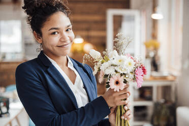 Smiling young businesswoman with flowers in office - JOSEF10783