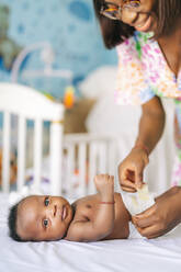 Smiling mother changing diaper of baby boy at home - OCMF02489