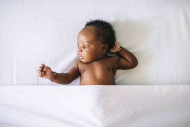Cute shirtless baby boy lying on bed under sheet at home - OCMF02491