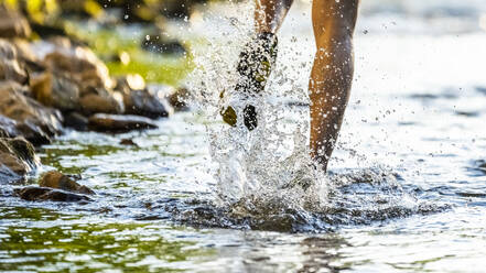 Mann läuft durch einen Fluss und spritzt Wasser - STSF03254