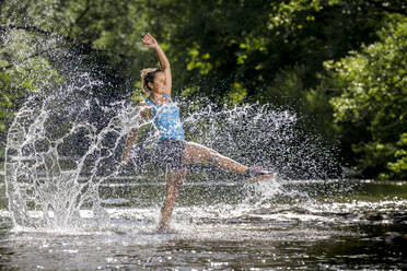 Junge Frau spritzt im Fluss stehend Wasser - STSF03258