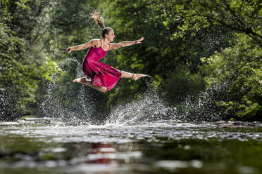 Woman with arms outstretched jumping over river - STSF03260