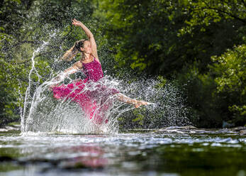 Junge Frau im Kleid, die im Fluss Wasser spritzt - STSF03261