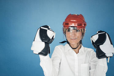 Businesswoman wearing gloves and helmet against blue background - JOSEF10794
