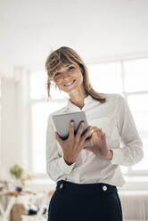 Smiling businesswoman with tablet PC standing in office - JOSEF10797