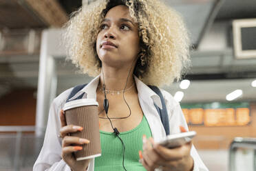 Thoughtful woman holding disposable cup and smart phone - JCCMF06595