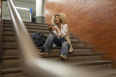 Happy woman using smart phone sitting on steps - JCCMF06601