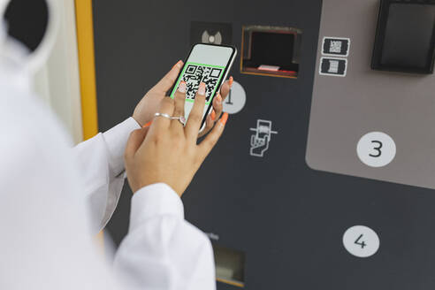 Woman scanning QR code through smart phone near ticket vending machine - JCCMF06607