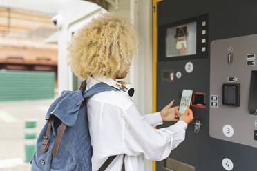Frau, die einen Fahrkartenautomaten benutzt und den QR-Code über ihr Smartphone scannt - JCCMF06608