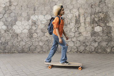 Junge Frau mit Rucksack auf dem Skateboard an der Wand - JCCMF06618