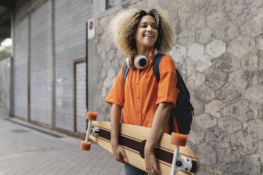 Junge Frau mit Skateboard an der Wand stehend - JCCMF06620