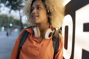 Contemplative woman with headphones by illuminated banner - JCCMF06638