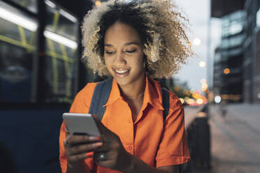 Junge Frau mit lockigem Haar, die nachts ihr Smartphone benutzt - JCCMF06656