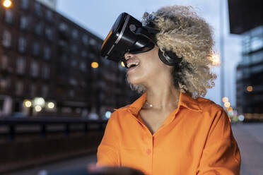 Glückliche Frau mit Virtual-Reality-Headset bei Nacht - JCCMF06658