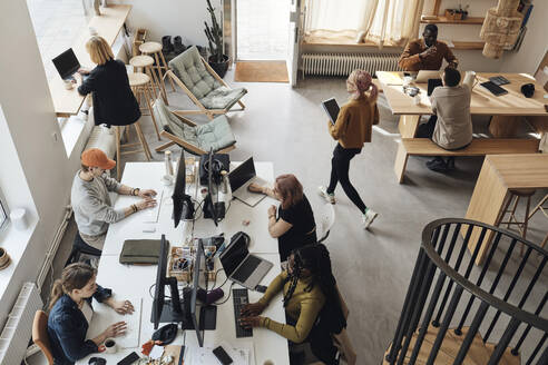 Blick von oben auf männliche und weibliche Unternehmer, die im Büro eines Tech-Start-ups arbeiten - MASF30853