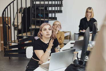 Young female computer programmer discussing with colleague during business meeting in office - MASF30872