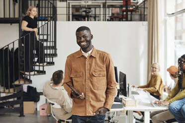 Portrait of smiling male programmer holding digital tablet while standing at tech start-up office - MASF30884