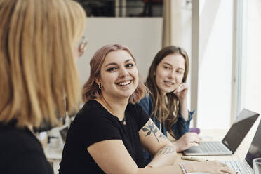 Lächelnde Unternehmerinnen, die einen Kollegen während einer Besprechung im Büro ansehen - MASF30888