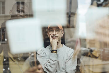 Nachdenklicher männlicher Programmierer mit Blick auf Haftnotizen am Fenster im Büro eines Start-up-Unternehmens - MASF30910