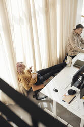 Hohe Winkel Ansicht der nicht-binären Unternehmer mit Füßen auf dem Schreibtisch von männlichen Kollegen im Büro - MASF30935