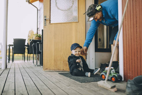 Lächelnder Vater spielt mit seinem auf der Fußmatte sitzenden Sohn auf der Veranda - MASF31069