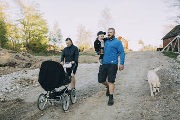 Family walking with dog and baby stroller on dirt road - MASF31074