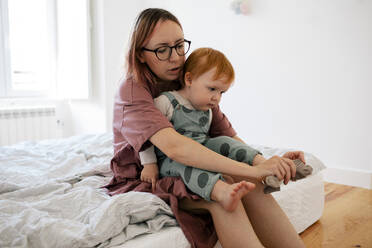 Mutter legt Socke an den Fuß eines männlichen Kleinkindes im Schlafzimmer - MASF31095