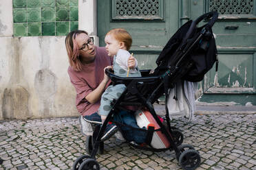 Mutter sieht weinenden Sohn im Kinderwagen auf dem Gehweg sitzend an - MASF31099