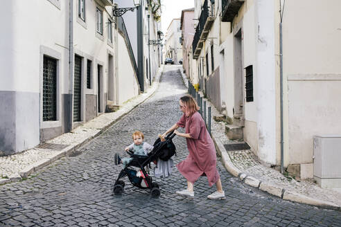 Mutter geht mit männlichem Kleinkind im Kinderwagen auf der Straße spazieren - MASF31100