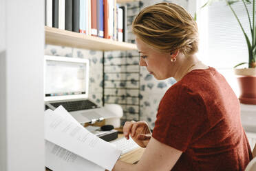 Geschäftsfrau prüft Dokumente am Schreibtisch bei der Arbeit von zu Hause aus - MASF31106