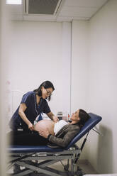 Weiblicher Gesundheitsexperte misst den Bauch einer schwangeren Frau, die auf einer Trage in einer medizinischen Klinik liegt - MASF31161