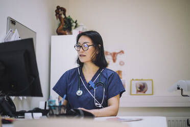 Reife Ärztin mit Brille am Computer sitzend am Schreibtisch im Krankenhaus - MASF31165