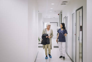 Ältere Frau in voller Länge im Gespräch mit einer Ärztin auf dem Gang in einer medizinischen Klinik - MASF31169