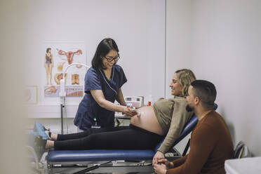 Lächelnder Gynäkologe bei der Ultraschalluntersuchung einer schwangeren Frau, die von einem Mann im Krankenhaus betreut wird - MASF31203