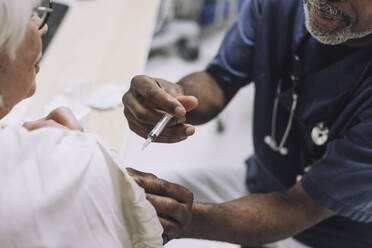 Male doctor injecting senior female patient in medical clinic - MASF31218