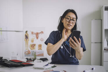 Weibliche HNO-Ärztin bei der Online-Konsultation über das Mobiltelefon, während sie am Schreibtisch in einer medizinischen Klinik sitzt - MASF31242