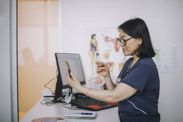 Ärztin bei der Diskussion über ein Reagenzglas während einer Online-Konsultation über ein Mobiltelefon im Krankenhaus - MASF31243