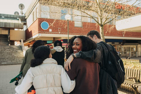 Rear view of smiling girl looking over shoulder while walking with friends at street - MASF31247