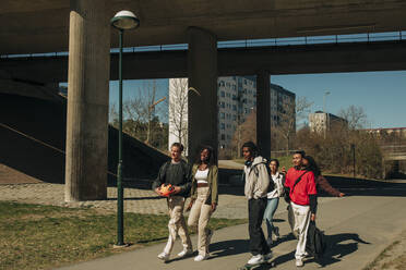 Multiracial männlichen und weiblichen Freunde zu Fuß zusammen auf der Straße während sonnigen Tag - MASF31256