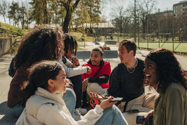 Multiracial male and female friends talking while sitting together at park - MASF31262