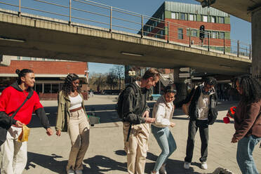 Multiracial friends looking at young woman dancing at street on sunny day - MASF31278