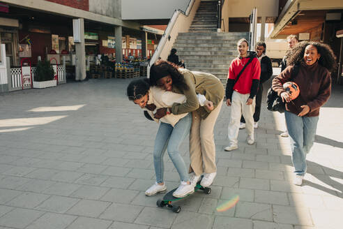 Verspielte Freundinnen stehen auf einem Skateboard auf der Straße - MASF31282