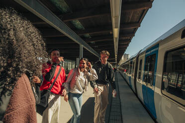 Multirassische spielerische Freunde stehen in der Nähe des Zuges am Bahnhof - MASF31286