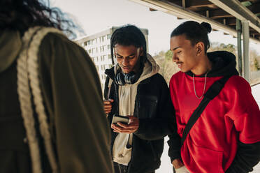 Junger Mann teilt sein Smartphone mit einem Freund, während er am Bahnsteig spazieren geht - MASF31288