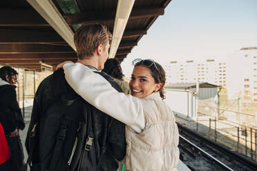 Porträt einer lächelnden Frau, die den Arm um einen Freund legt, der auf einem Bahnhof spazieren geht - MASF31291