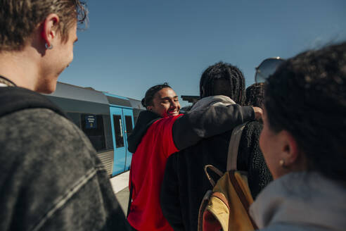 Lächelnder Mann schaut über die Schulter und legt den Arm um einen Freund am Bahnhof - MASF31297