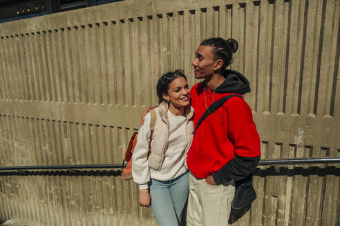 Lächelnde junge Frau steht mit einem männlichen Freund an einer Wand an einem sonnigen Tag - MASF31331