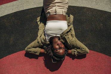 Carefree young woman with hands behind head relaxing in playground on sunny day - MASF31343