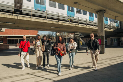 Happy multiracial young friends walking together on street below bridge - MASF31348